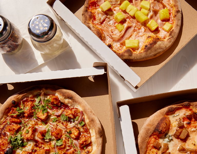Three pizzas in open boxes sit on a table with salt and pepper shakers nearby.